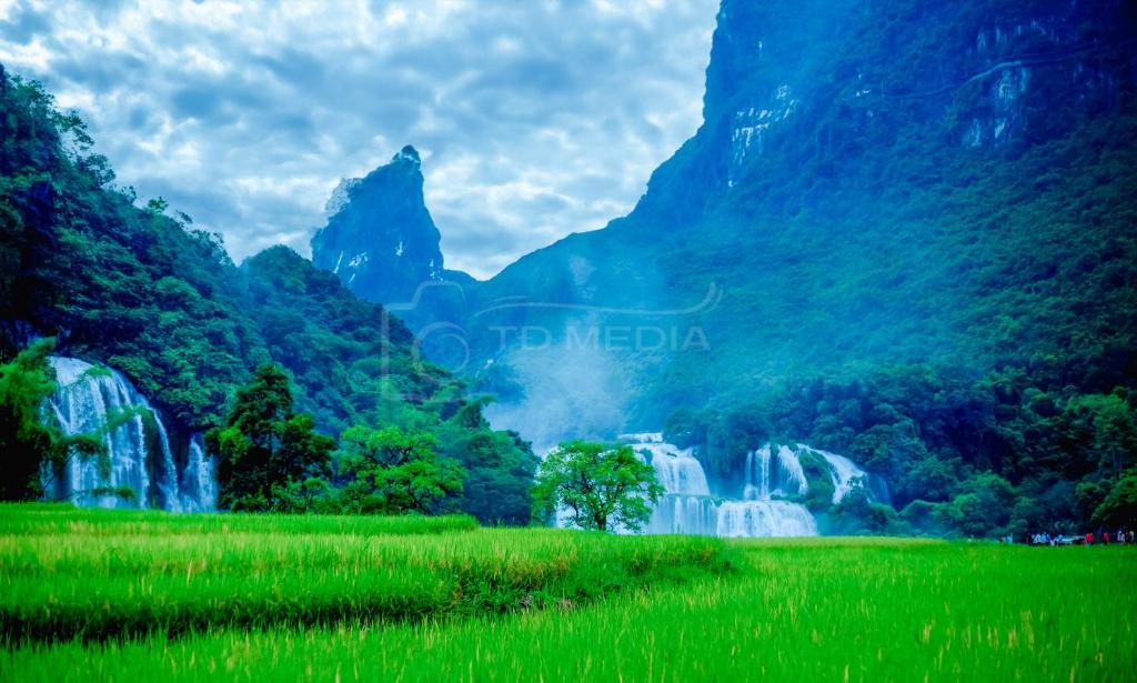 een groen veld met waterval en bergen op de achtergrond bij Khách Sạn Bản Giốc Quây Sơn in Lũng Niêo