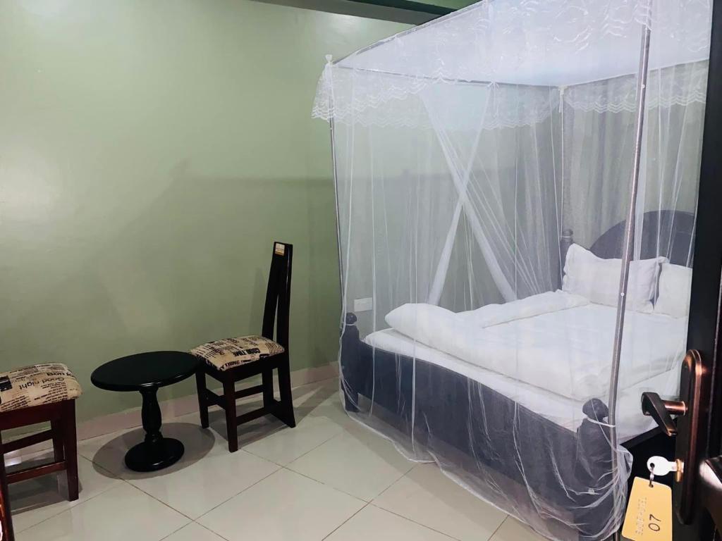 een slaapkamer met een hemelbed met een tafel en een kruk bij Suzie hotel in Kampala