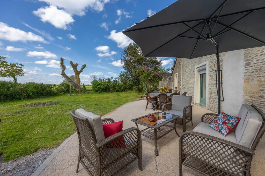 un patio avec une table, des chaises et un parasol dans l'établissement Izéla, à Cricqueville-en-Bessin