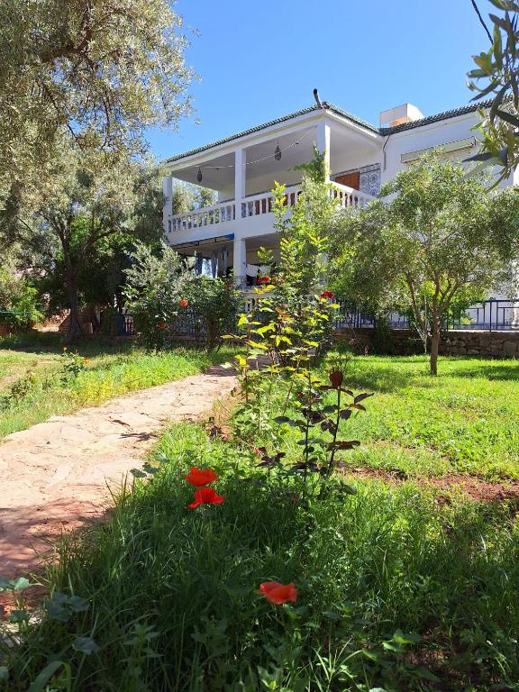 a large white house with red flowers in the grass at Maison Touria in Ouzoud