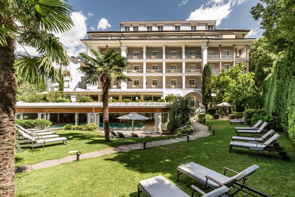 an exterior view of a hotel with lawn chairs and palm trees at Classic Hotel Meranerhof in Merano
