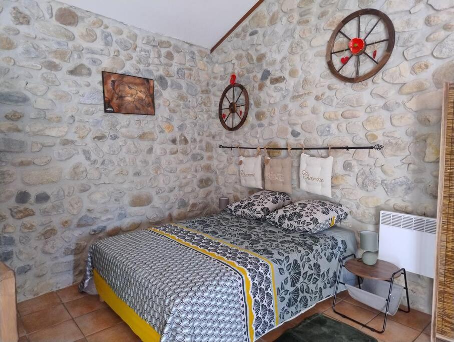 1 dormitorio con cama y pared de piedra en lou caladou gîte en pierre avec bain à remous, en Vallon-Pont-dʼArc