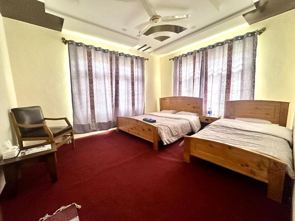 two beds in a room with a chair and window at Indus Cabana Guest House and resort in Skardu