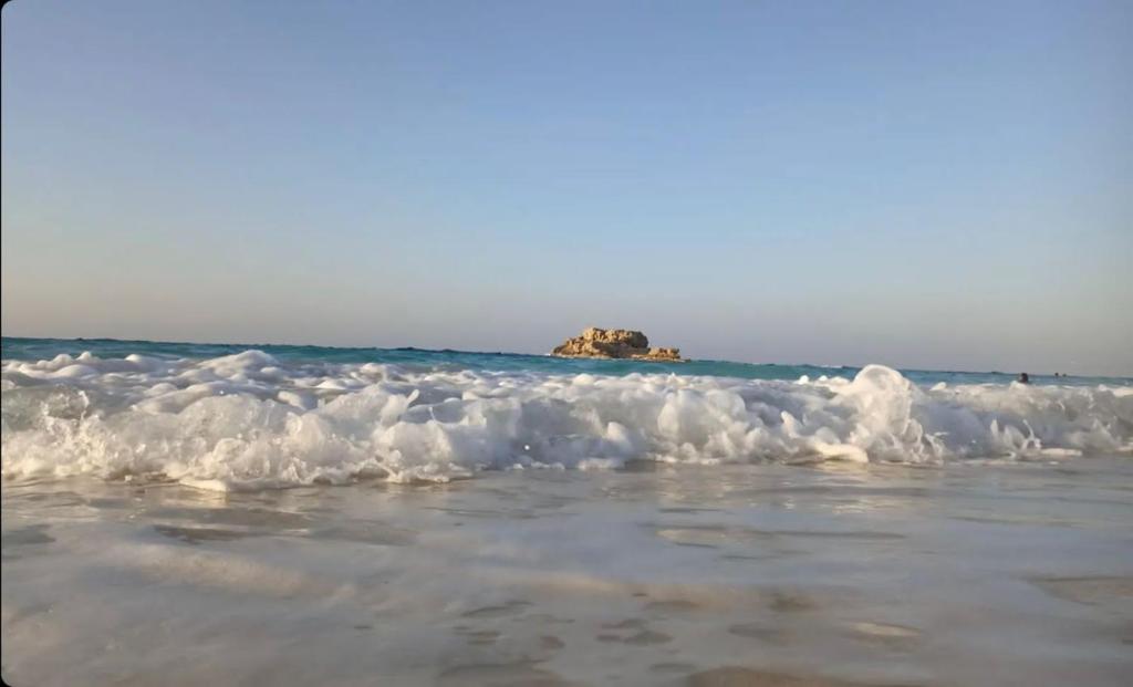 a beach with waves and a rock in the ocean at شقه مصيف للايجار بكمبوند عجيبه سيتي مرسي مطروح in Zâwyet Umm el Rakham