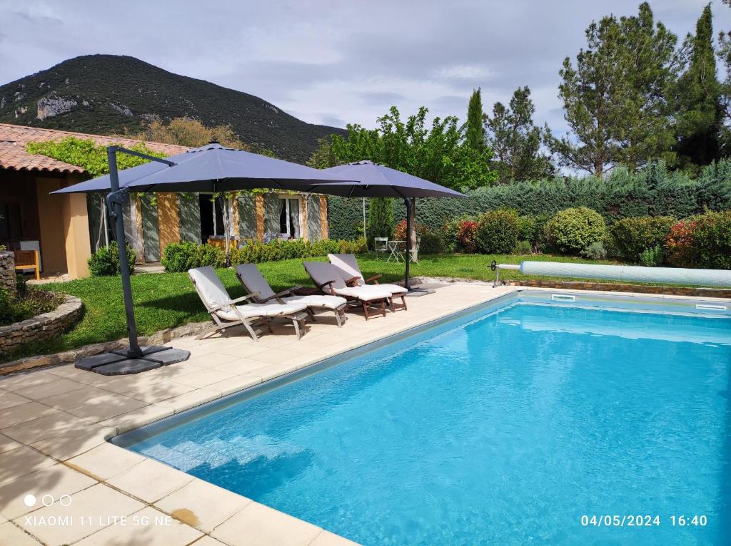 - une piscine avec 2 chaises et un parasol dans l'établissement GITE AUX 4 SAISONS DU COLORADO PROVENÇAL - 3 ÉTOILES - Rustrel, à Rustrel