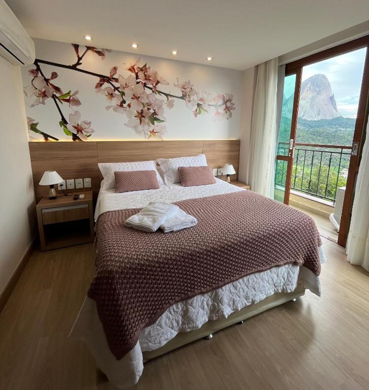 a bedroom with a large bed with a flowering tree on the wall at Vista da Pedra Flat em Pedra Azul in Pedra Azul