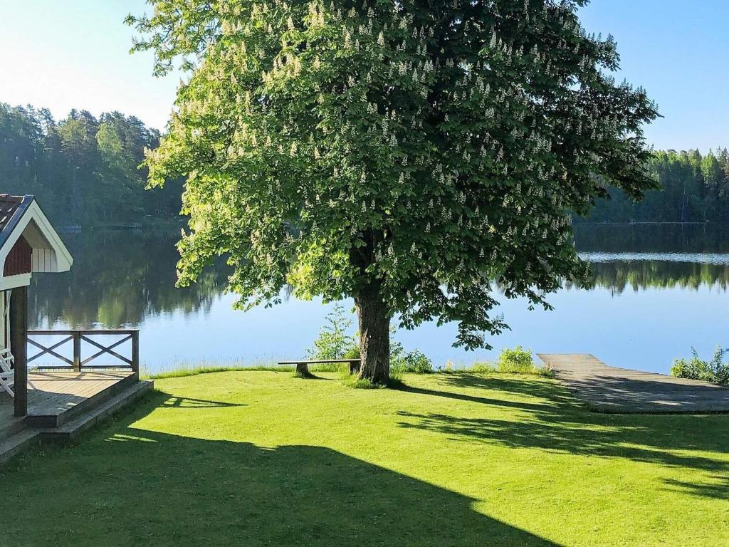 uma árvore sentada na relva ao lado de um lago em Holiday home STENSJÖN em Boda
