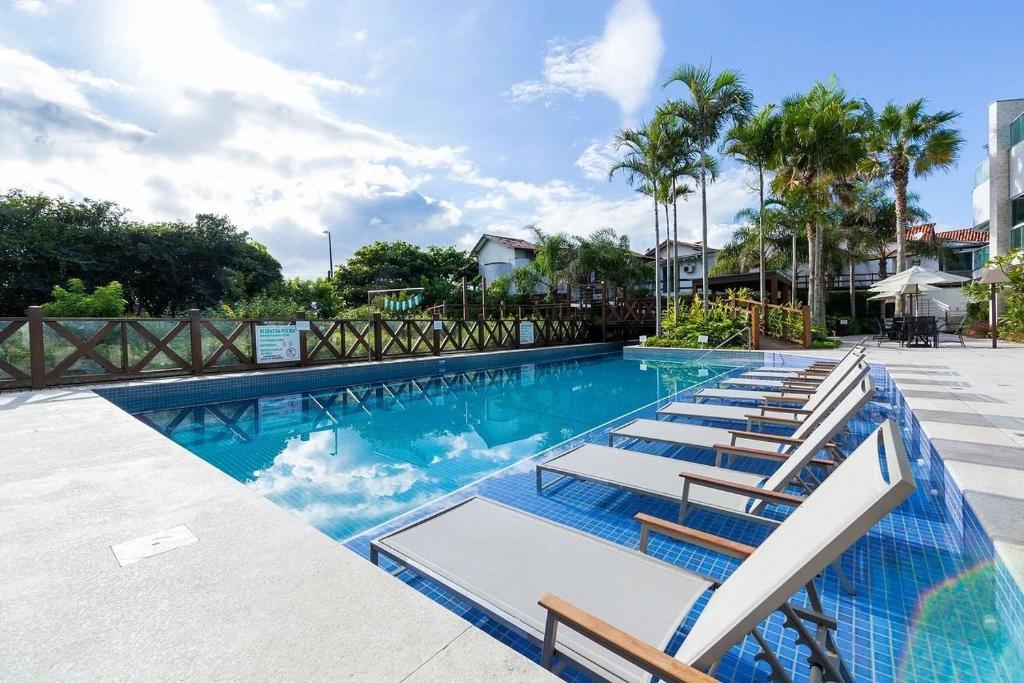 a large swimming pool with lounge chairs and palm trees at Varandas do Atlântico 306A - Excelente apartamento em condomínio de luxo a beira mar - Piscina climatizada - Academia - (Consultar serviços de roupas de cama e banho) in Bombas