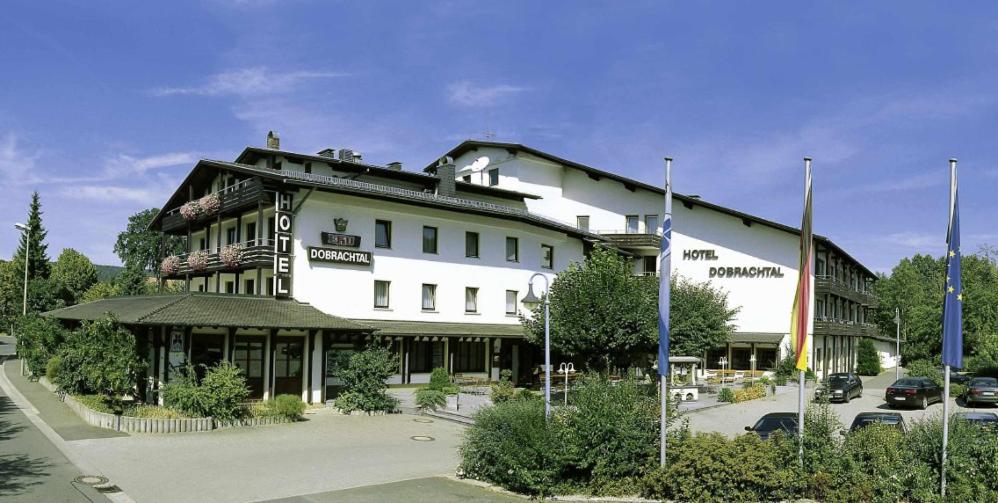 un grand bâtiment blanc avec des voitures garées dans un parking dans l'établissement Flair Hotel Dobrachtal, à Kulmbach