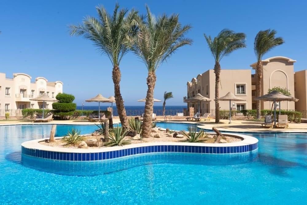 a swimming pool with palm trees in a resort at Sunset pearl Sahl Hashesh in Hurghada