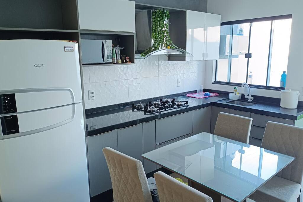 kuchnia ze szklanym stołem i białą lodówką w obiekcie Casa aconchegante Gran Ville w mieście Rondonópolis