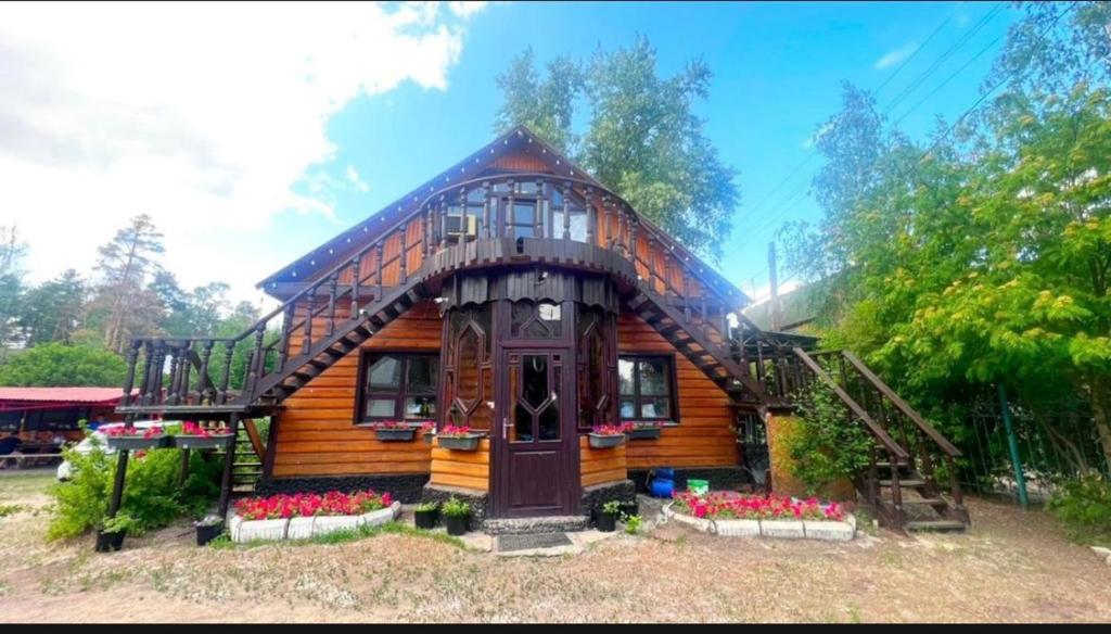 una pequeña casa de madera con flores delante en Гостевой дом ОЛЖАС en Borovoye