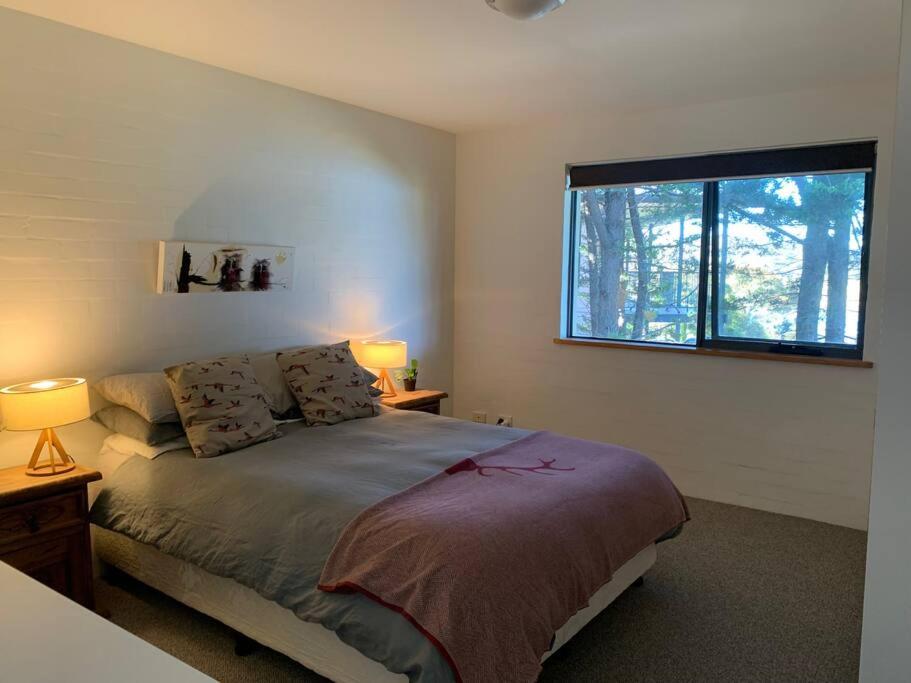 a bedroom with a bed with two lamps and a window at Apartment minutes to Lake in Jindabyne