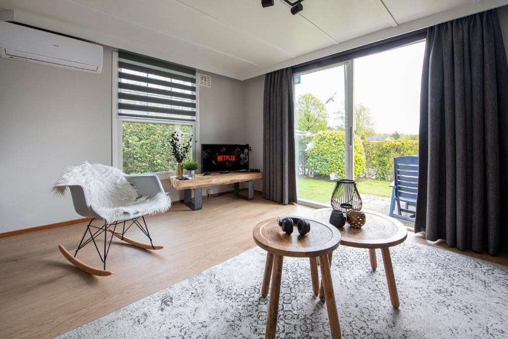 a living room with a large window and a chair and tables at 37, located in a quiet & wooded area! in Oisterwijk
