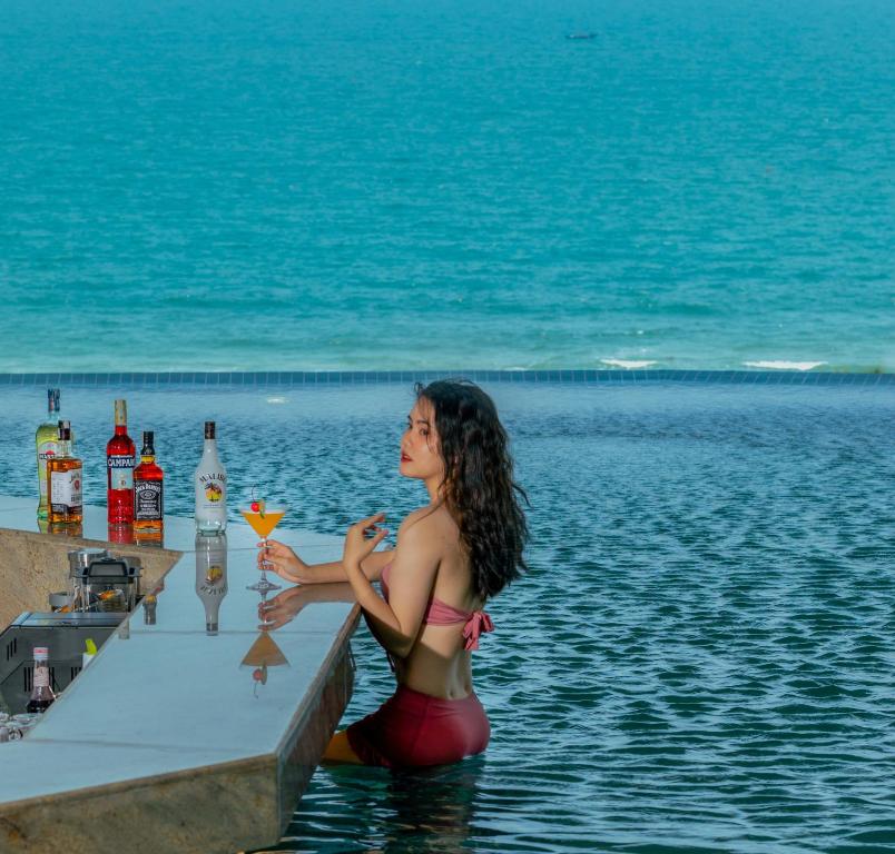 a woman sitting in the water holding a drink at Awaken Da Nang Hotel in Danang