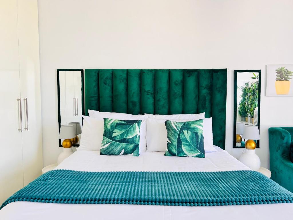 a bedroom with a white bed with a green headboard at City junction studio apartment in Windhoek