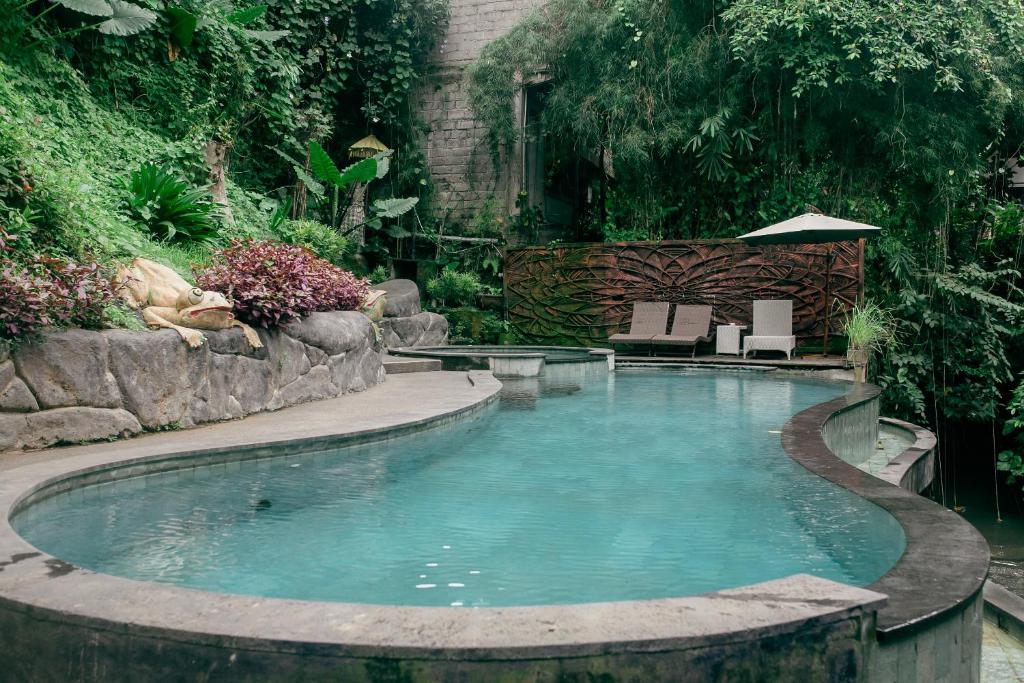 a swimming pool in a garden with two chairs and an umbrella at Kubuku Ubud Villas in Ubud