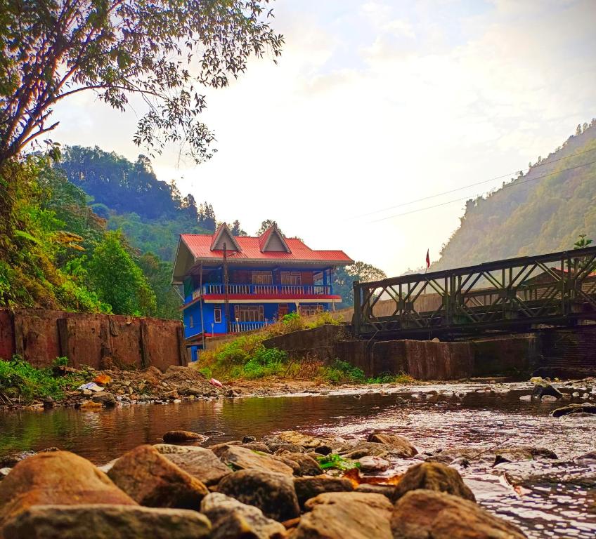 a blue building next to a river with a bridge at Sikkim Silk Route Riverside Resort, Rongli in Rongli