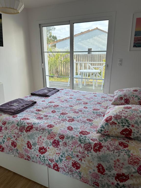 a bedroom with a bed with a floral comforter and a window at Villa MA&amp;VA in Lacanau-Océan