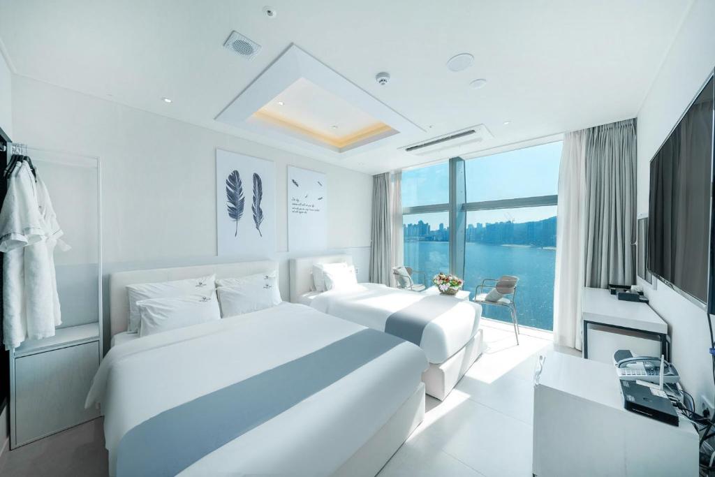 two beds in a white room with a large window at Oceanstay Hotel in Busan