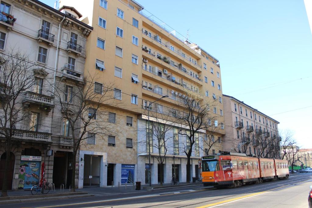 Un autobus rosso che guida lungo una strada accanto a un palazzo alto di Hotel America a Milano