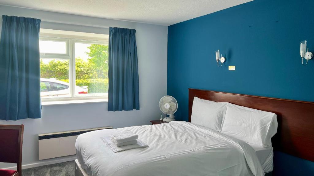 a bedroom with a bed with blue walls and a window at MK Hotel in Stony Stratford