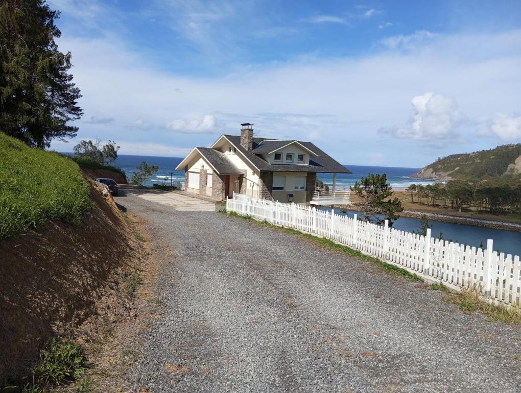 una casa en una colina al lado de una valla blanca en LA VILLA DE MARIA -CASA MONICA Y GEORGE PLAYA DEL PUNTAL Planta Baja CASA ADOSADA en Villaviciosa ASTURIAS en Villaviciosa