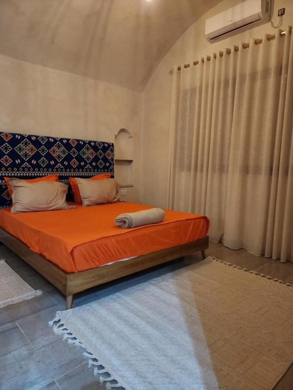 a bedroom with a bed with orange sheets and a window at دار عزيزي in El Guecheïne