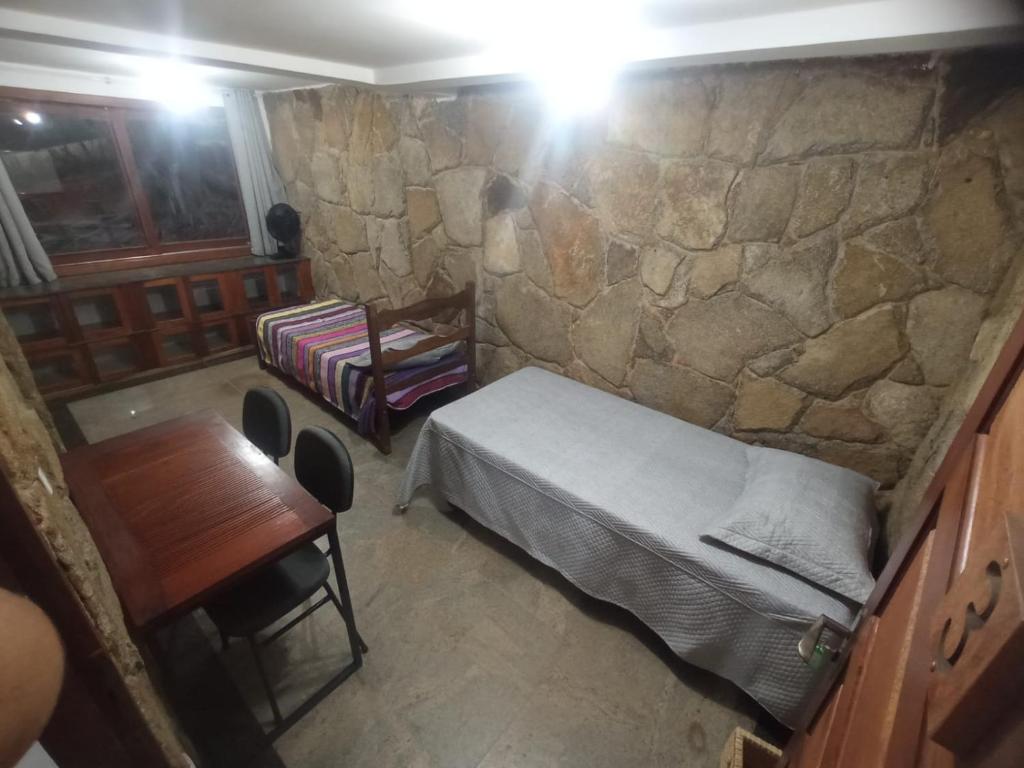Zimmer mit einem Bett, einem Tisch und einer Steinmauer in der Unterkunft Casa da Floresta in Lavras