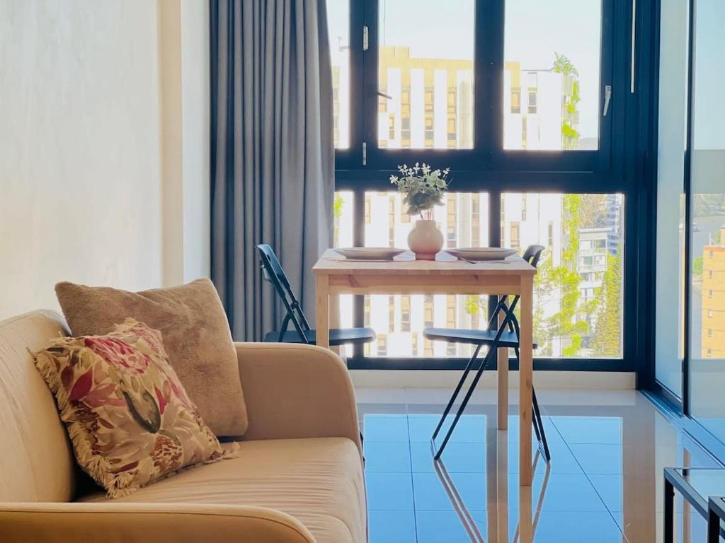 uma sala de estar com um sofá, uma mesa e janelas em CASSA TOOWONG - Convenient 1B Apt at Central Location with Parking Managed by The Cassa em Brisbane
