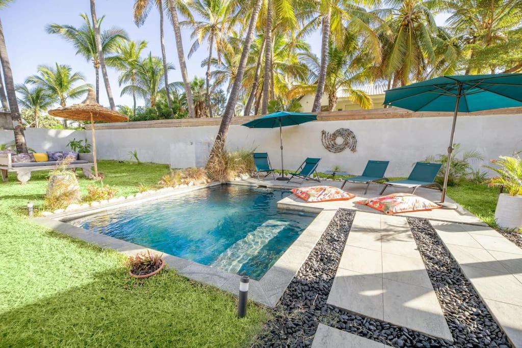 a pool with chairs and umbrellas in a backyard at Villa Nauraa - 5ch - piscine - proche plage. in Trois Bassins