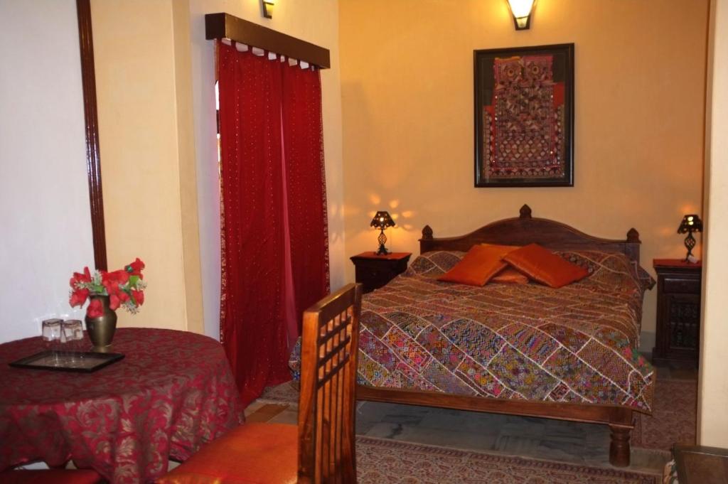 - une chambre avec un lit avec des rideaux rouges et une table dans l'établissement Killa Bhawan Lodge, à Jaisalmer