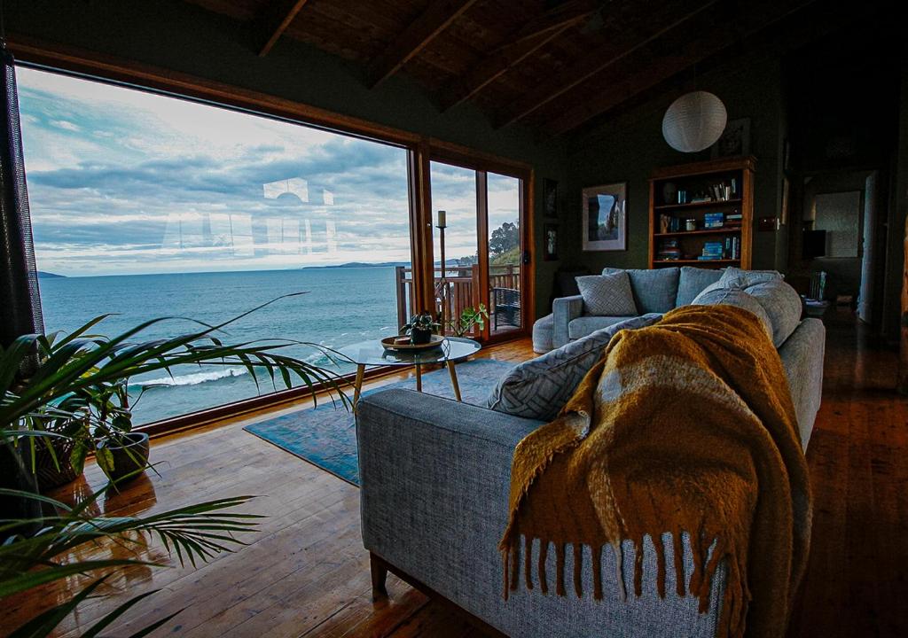 ein Wohnzimmer mit Couch und Blick aufs Meer in der Unterkunft Waterfront - Bluff Beach House, Park Beach in Dodges Ferry