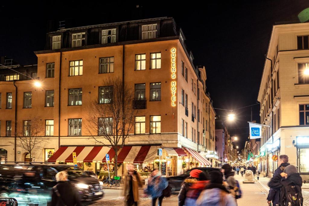 a group of people walking down a city street at night at Queen's Hotel by First Hotels in Stockholm