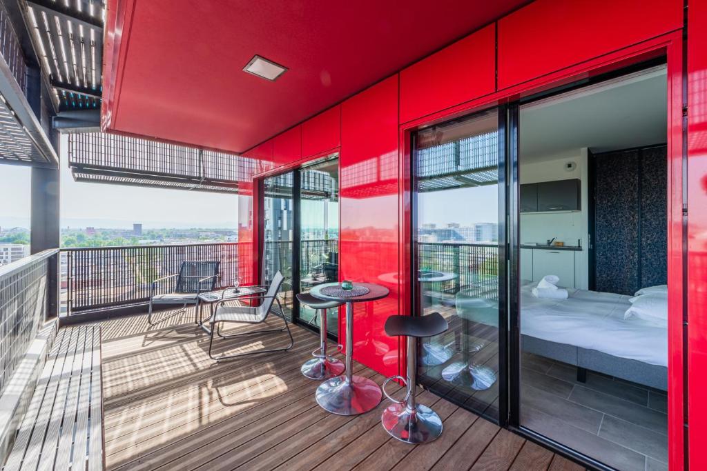 un balcon avec des murs rouges et un lit et des tabourets dans l'établissement Red Sky - Studio presquîle Malraux avec terrasse, à Strasbourg
