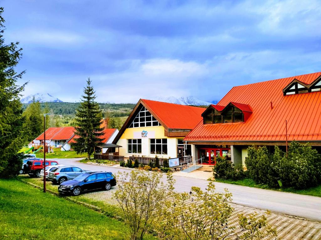 un bâtiment avec un toit orange et des voitures garées devant dans l'établissement Hotel RYSY, à Tatranska Strba