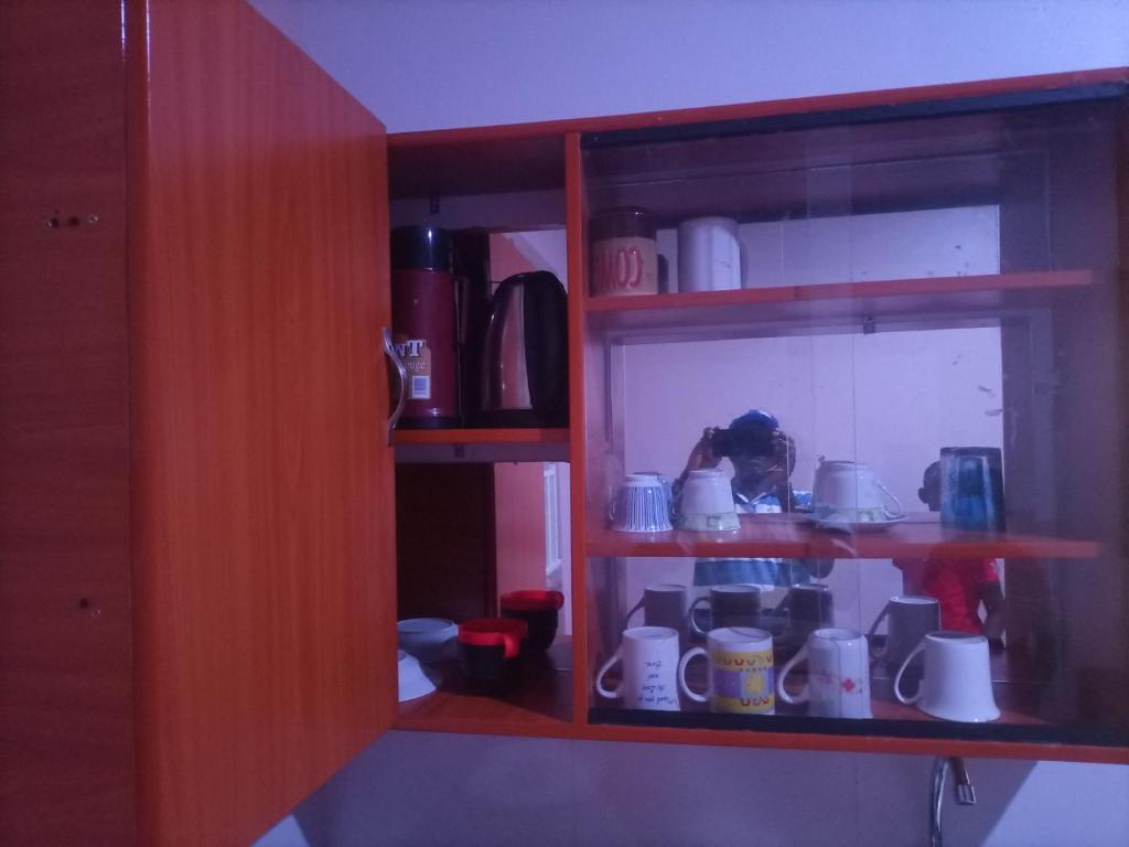 un estante con tazas y otros artículos. en Pearl Furnished Rooms Buloba, en Kampala