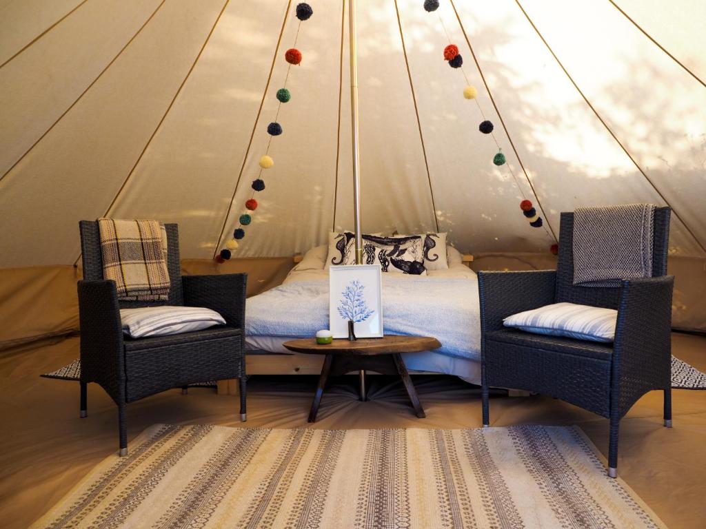 a bed in a tent with two chairs and a table at Foxglove Field Glamping in Perranuthnoe