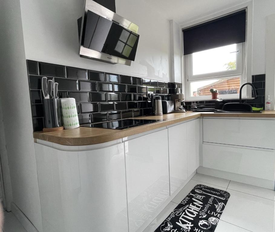 a kitchen with white cabinets and black tile on the wall at Two bedroom ground floor apartment with garden in Falkirk