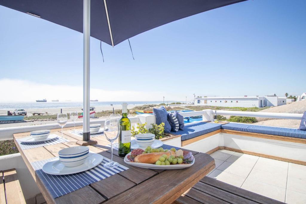a table with a plate of food on a balcony with the beach at Tides Holiday Home in Paternoster