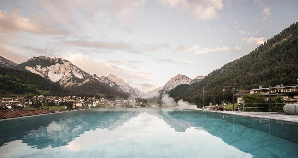 a pool of water with mountains in the background at Excelsior Dolomites Life Resort in San Vigilio Di Marebbe