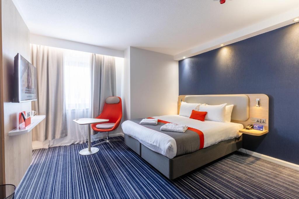 クロイドンにあるホリデイ イン エクスプレス ロンドン クロイドンのベッドと赤い椅子が備わるホテルルームです。