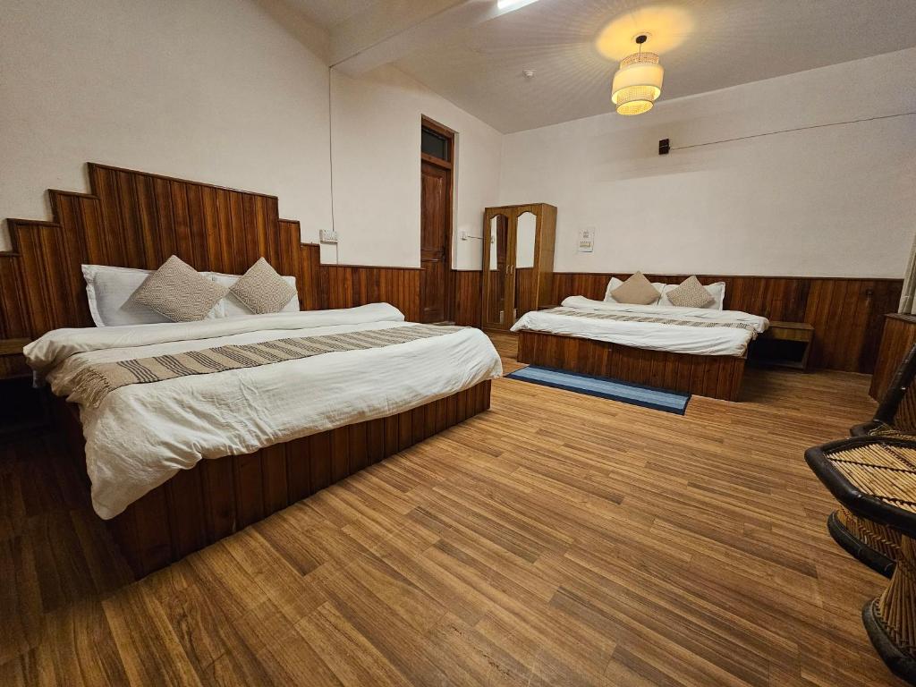 two beds in a hotel room with wooden floors at Drifters Inn - The Hidden Tribe in Manāli