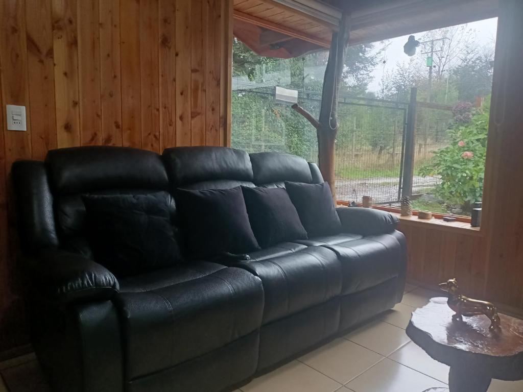a black leather couch in a living room with a window at Cabaña Beatriz in Coñaripe