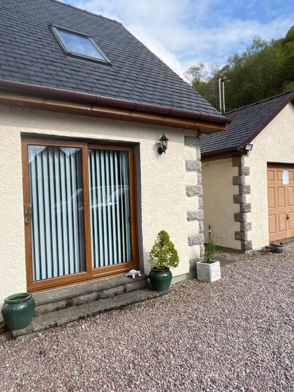 a house with a wooden door and two potted plants at Tigh na Drochaid, Glen Nevis - Entire Apartment in Fort William
