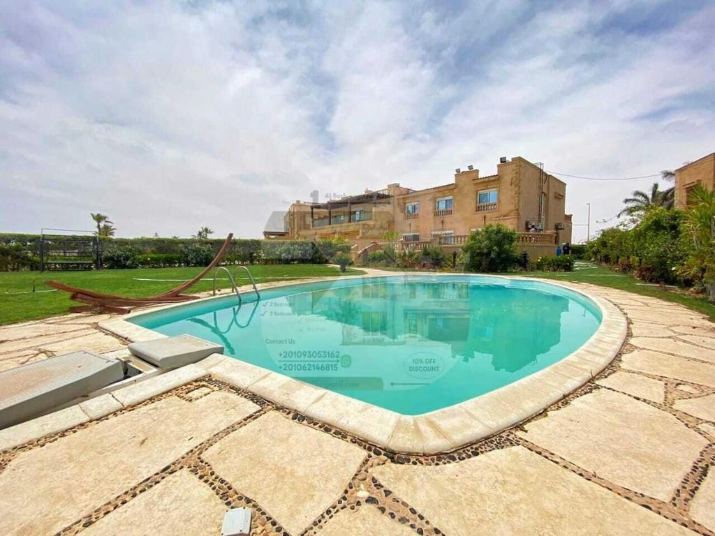 una piscina en un patio con un edificio en el fondo en Villa with a charming view, sea view, Marina en El Alamein
