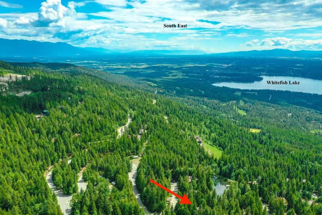 ホワイトフィッシュにあるPtarmigan Hilltop Hideawayの山の湖を指し示す赤い矢印が付いた森林の航空写真