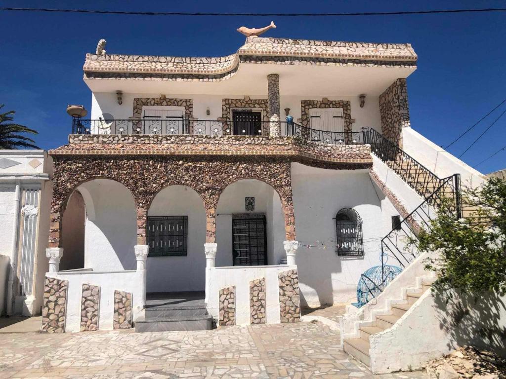 a white house with a balcony and stairs at Villa Neji, Havre de pierre à 10 min de la plage. in Korba