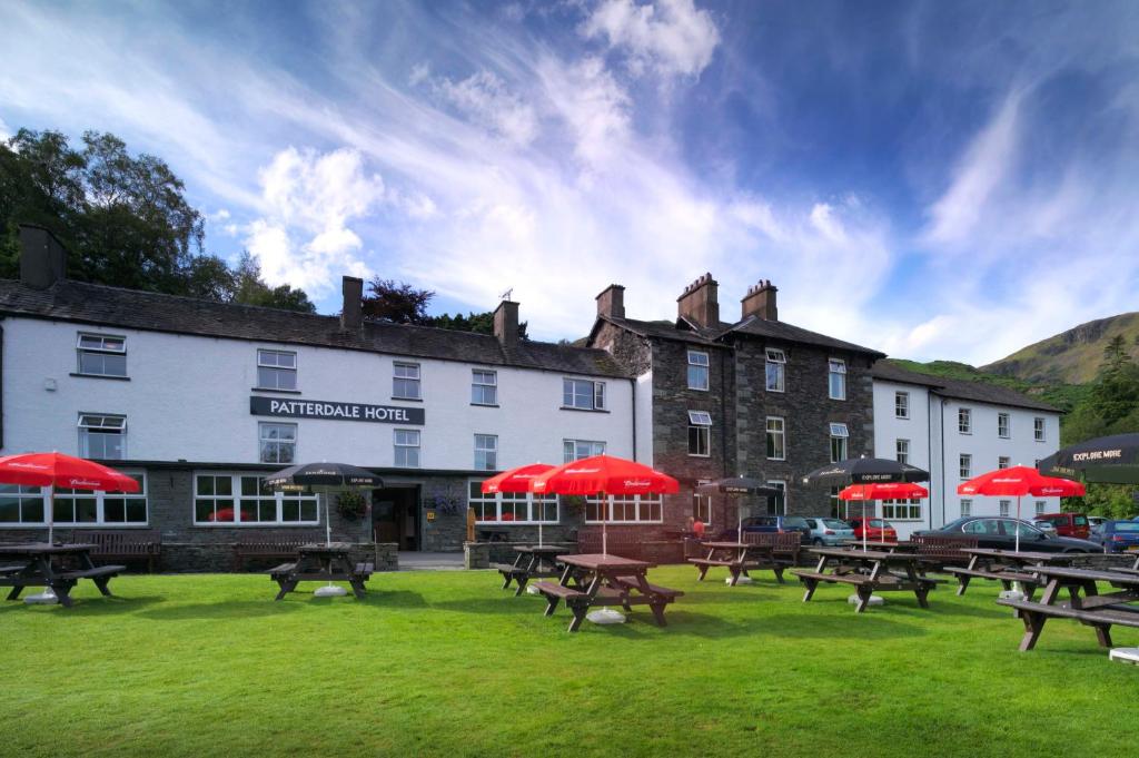 un hotel con mesas de picnic y sombrillas rojas en la hierba en Patterdale Hotel en Patterdale