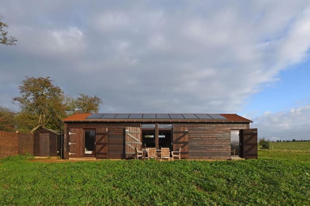 a small house with a solar roof on a field at Architect-designed Suffolk Barn, spectacular view in Blythburgh